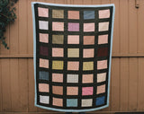 hanging quilt with brickwork-like pattern, made with brown, blue and pink fabrics