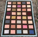 quilt with brickwork-like pattern, made with pink, brown and blue fabrics, laying on the ground