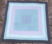 quilt in a housetop style, made from blue and green fabrics, laying flat on the ground